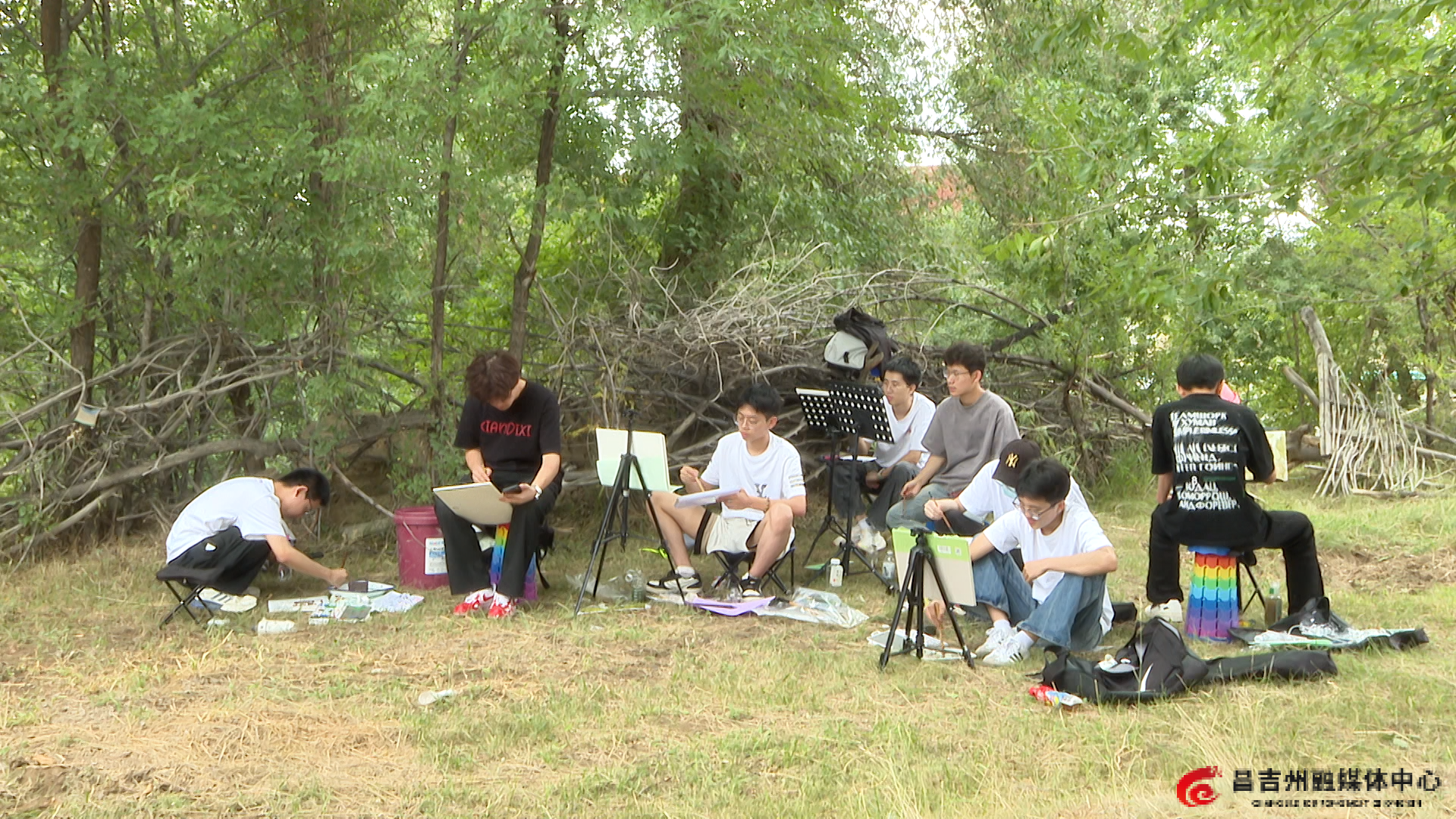 在天然草地上，学生们有的盯着树木调色、有的正在构思如何描绘，都在低头专注作画。叶钰摄.png