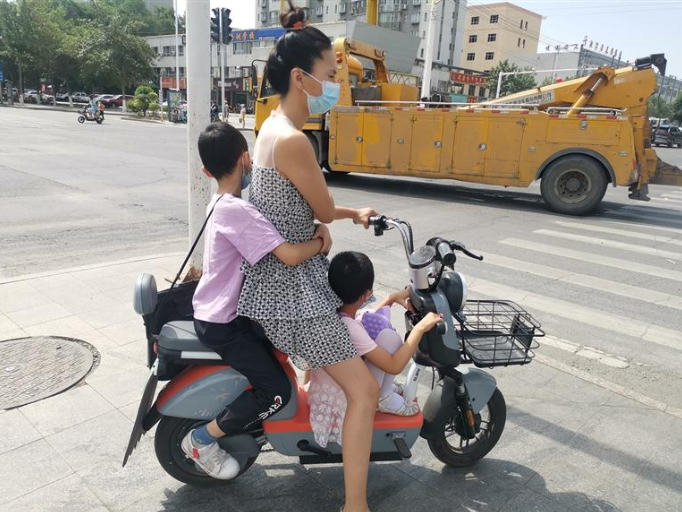 一位女士骑电动车时带了两个孩子,一个孩子坐在电动车后座上,另一个则
